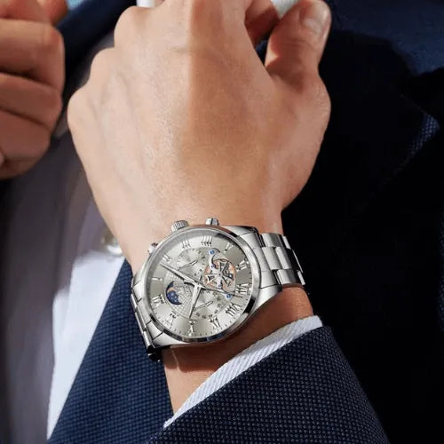 Elegant men’s silver stainless steel watch with moon phase dial, chronograph sub-dials and luminous Roman numerals, worn with a formal suit.