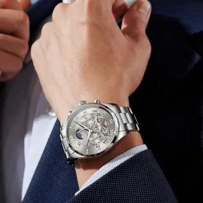 Elegant men’s silver stainless steel watch with moon phase dial, chronograph sub-dials and luminous Roman numerals, worn with a formal suit.